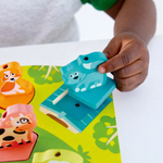 Child's hand holding a blue animal-shaped puzzle piece over a colorful puzzle with animal illustrations.