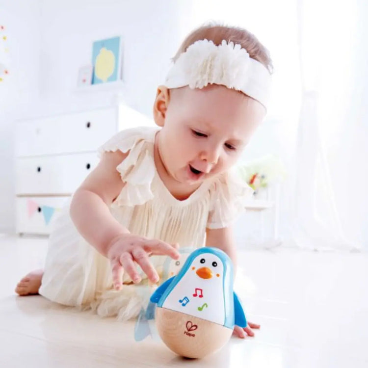 Baby playing with Hape Penguin Musical Wobbler – safe, non-toxic wooden toy that makes soft tinkling sounds, available in Kenya from Cheza Plus.