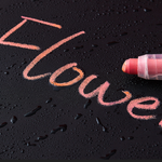 Pink chalk writing on a black surface with a pink chalk stick.