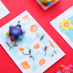 Children's art project with a flower design and a colorful printing tool on a red background.